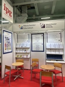 London Book Fair booth with two round tables, red carpeted floor and 2 white walls holding sales materials.